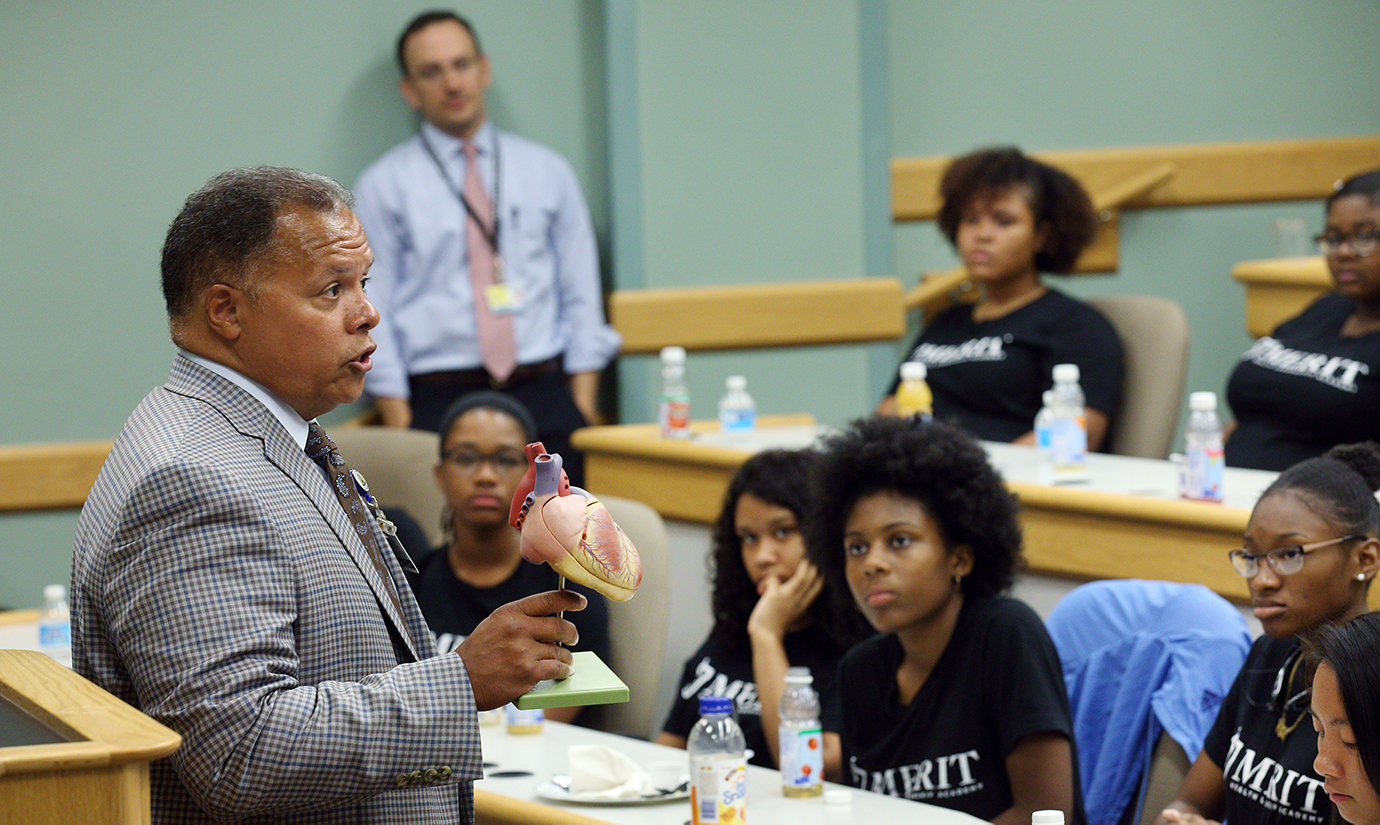 Robert Higgins, holding up a plastic model of the human heart, speaks to a classroom of high school students.